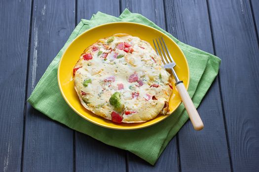 Hearty and tasty breakfast, traditional in the hotel, omelette from chicken eggs with cheese, fresh vegetables - cucumber and tomato on the black wooden background