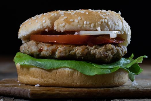 Roll with roast cutlet. Hamburger on a wooden board. Kitchen table, black background.