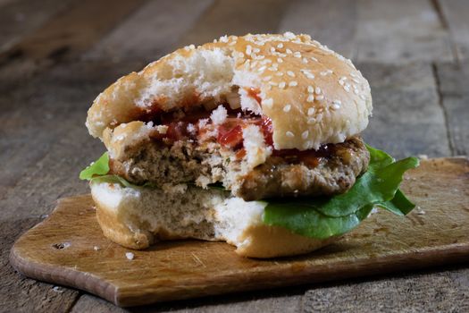 Roll with roast cutlet. Hamburger on a wooden board. Kitchen table, black background.