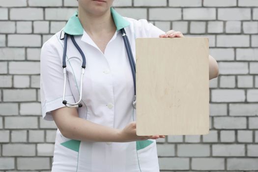 Medicine concept doctor. collection of information. The woman is holding an empty wooden plaque under the text. Against a brick wall background. Photo for your design