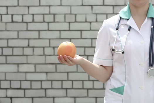 Medicine concept doctor. Diet and proper nutrition. Vitamin orange ripe. On a white brick wall background. Keeps the fruit. In the profile. Photo for your design
