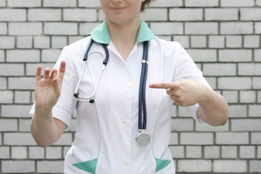 Medicine concept doctor. On a white brick wall background. Holds a pink pill. Advertising of products is indicated by a finger. Photo for your design