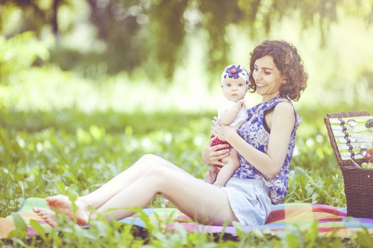 Young beautiful mother sits on blanket with her daughter during a picnic in the park