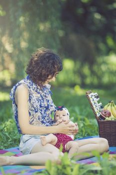 Young beautiful mother sits on blanket with her daughter during a picnic in the park