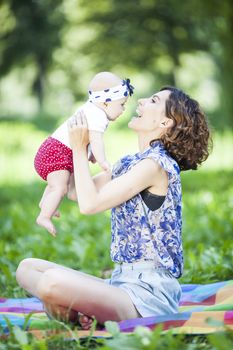 Young beautiful mother sits on blanket with her daughter during a picnic in the park