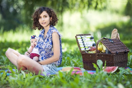 Young beautiful mother sits on blanket with her daughter during a picnic in the park