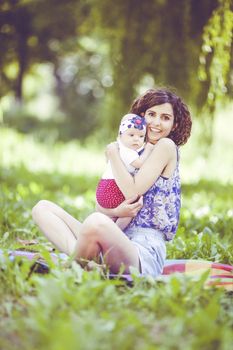 Young beautiful mother sits on blanket with her daughter during a picnic in the park