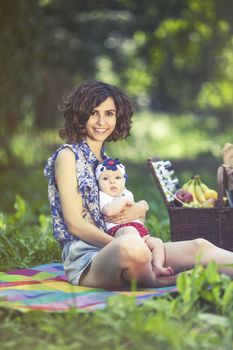 Young beautiful mother sits on blanket with her daughter during a picnic in the park