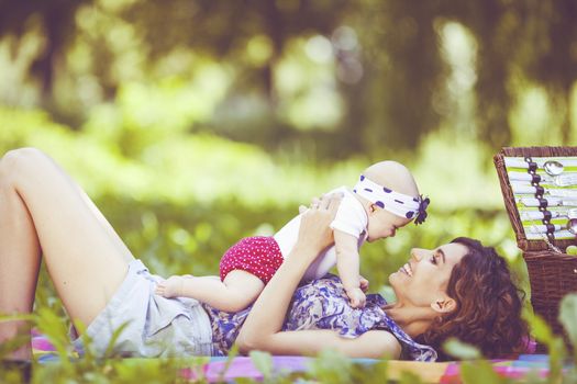 Young beautiful mother sits on blanket with her daughter during a picnic in the park