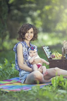 Young beautiful mother sits on blanket with her daughter during a picnic in the park