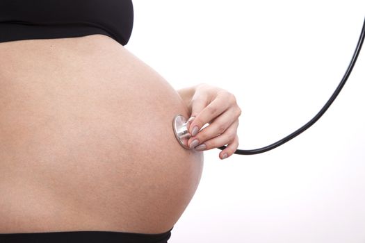 Pregnant woman listens to her child through a stethoscope.