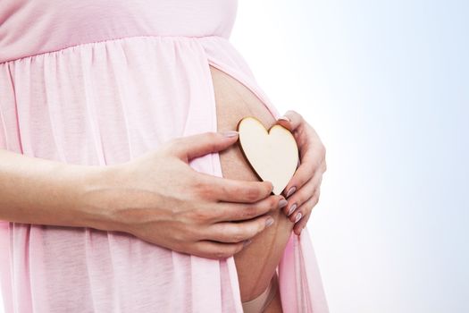 Pregnant woman puts heart on her belly.