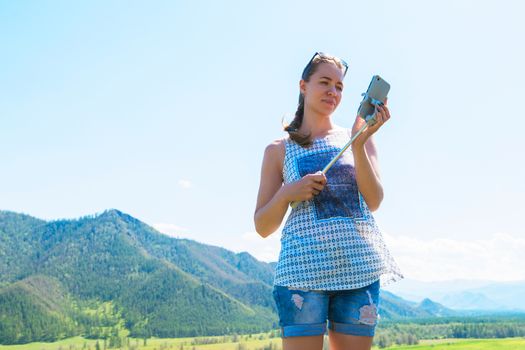 Woman taking selfie on mobile phone with stick. Vacation in the mountain