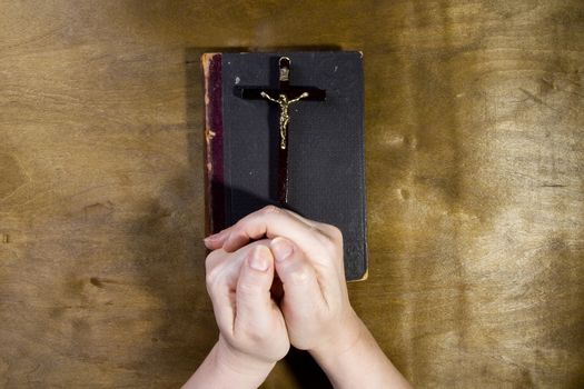 Female hands with a crucifix and an old book