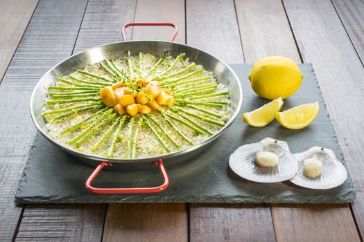 Paella with scollops and asparagus in traditional pan.