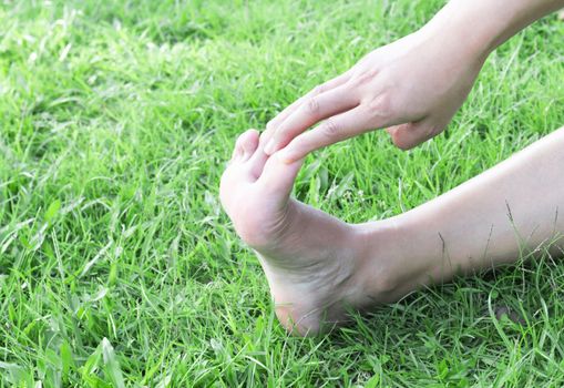 Woman stretching exercises feet finger on green grass background with light of sun, selective focus