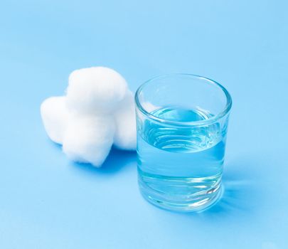Glass of blue alcohol and cotton wools on blue background for cleaning injured, health care and medical concept