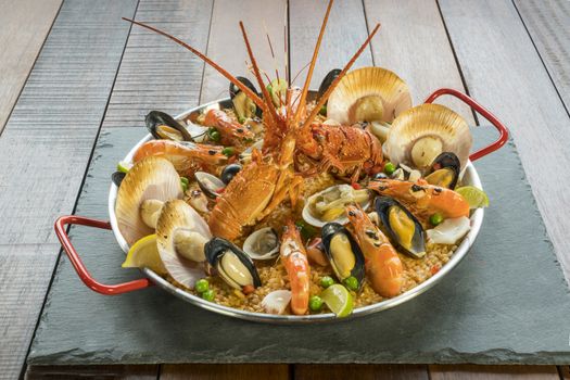 Gourmet seafood Valencia paella with fresh langoustine, clams, mussels and squid on savory saffron rice with prawn, scollops, mussels and lime slices, close up view