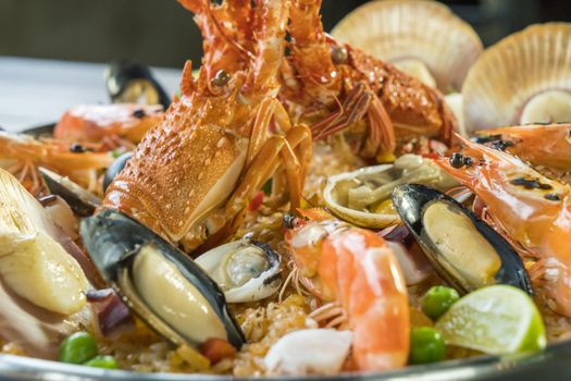 Gourmet seafood Valencia paella with fresh langoustine, clams, mussels and squid on savory saffron rice with prawn, scollops, mussels and lime slices, close up view