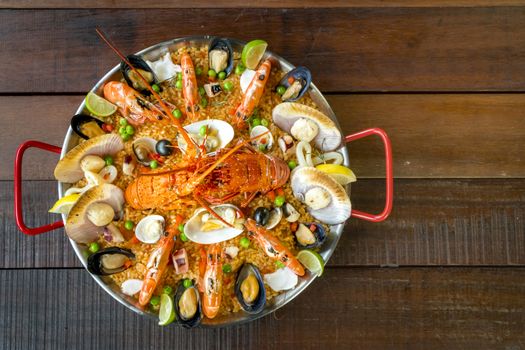 Gourmet seafood Valencia paella with fresh langoustine, clams, mussels and squid on savory saffron rice with prawn, scollops, mussels and lime slices, close up view