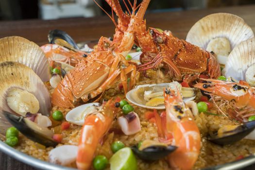 Gourmet seafood Valencia paella with fresh langoustine, clams, mussels and squid on savory saffron rice with prawn, scollops, mussels and lime slices, close up view