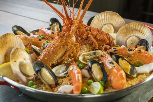 Gourmet seafood Valencia paella with fresh langoustine, clams, mussels and squid on savory saffron rice with prawn, scollops, mussels and lime slices, close up view
