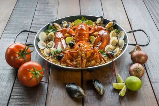 Gourmet seafood Valencia paella with fresh langoustine, clams, mussels and squid on savory saffron rice with peas and lemon slices, close up view