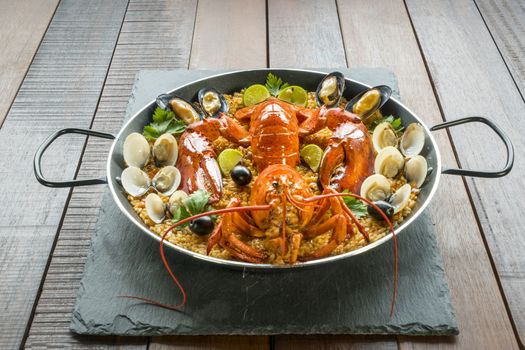 Gourmet seafood Valencia paella with fresh langoustine, clams, mussels and squid on savory saffron rice with peas and lemon slices, close up view