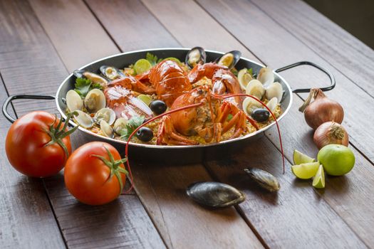 Gourmet seafood Valencia paella with fresh langoustine, clams, mussels and squid on savory saffron rice with peas and lemon slices, close up view