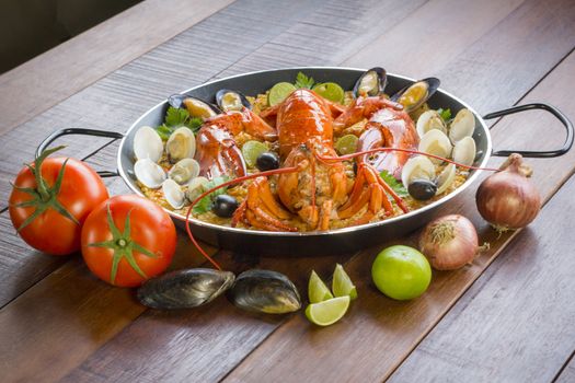 Gourmet seafood Valencia paella with fresh langoustine, clams, mussels and squid on savory saffron rice with peas and lemon slices, close up view