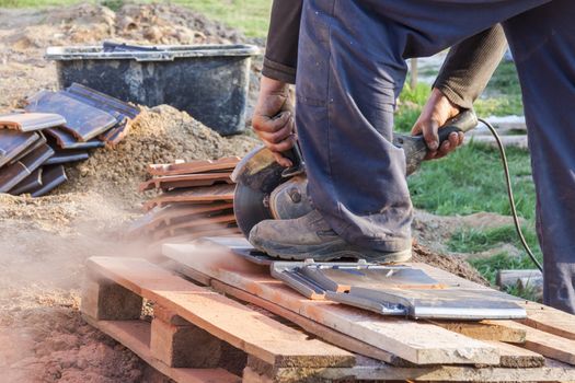 Worker using a hand circular saw to cut a roof-tile