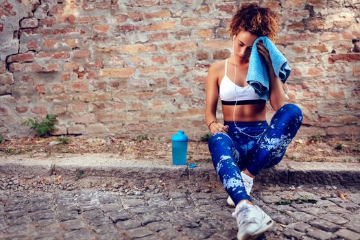 Young muscular woman with headphones resting after jogging.