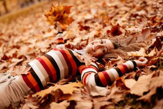 Beautiful young woman in sunny forest in autumn colors. She is lying on the ground covered with leaves and enjoying. 