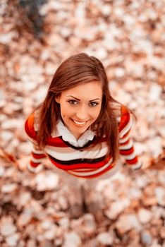 Top view of a beautiful young woman enjoying in forest in autumn colors. Looking at camera.