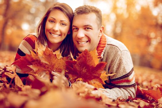 Beautiful young couple in sunny forest in autumn colors. They are lying on the falls leavess and looking at camera. 