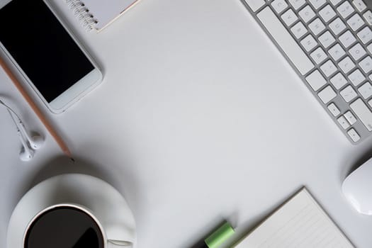 Top view with work space and copy space of white working table with keyboard, smartphone, cup of coffee and other supplies.