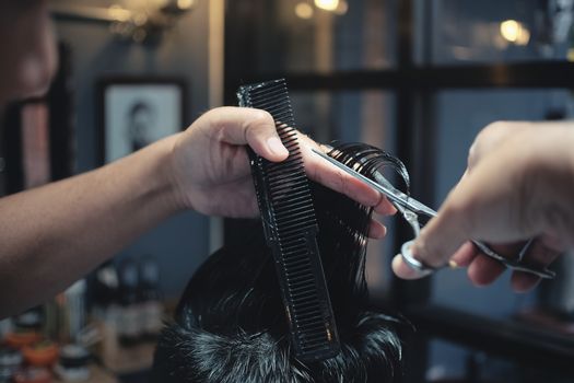 Hairdresser makes hairstyle a man with vintage tone.