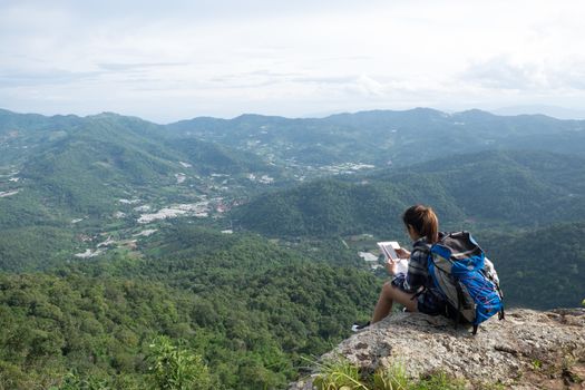 Young girl Hipster with backpack enjoying with smartphone on peak of foggy mountain. Tourist traveler on background view .Hiker in holiday trip in Thailand country.