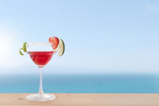 Red cocktail beverage with lime and ice by the coast