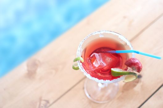 Red cocktail beverage with lime and ice by a swimming pool