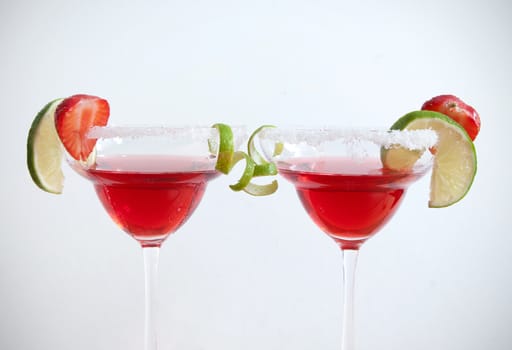 Two cocktail glasses with lime and strawberry slices over a white background