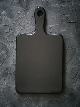 black wooden cutting board on black background.Empty black chop board for design, menu. Copy space. Vertical. Top view or flat lay.