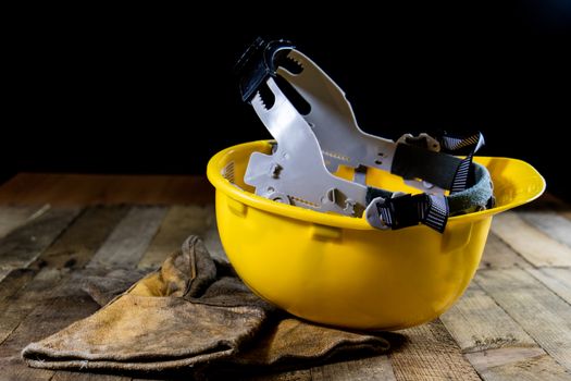 Yellow helmet and welding gloves. Black background and old wooden table.