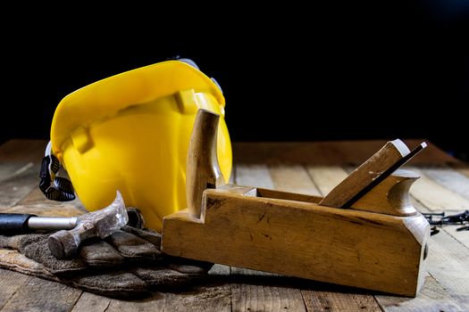 Yellow helmet and carpenter tools. Carpenter and old wooden table. Black background