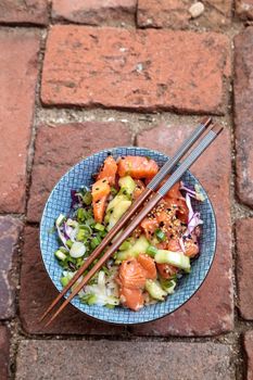 Raw salmon poke bowl with rice, cabbage, cucumber, sesame seeds and spring rolls with chopsticks.