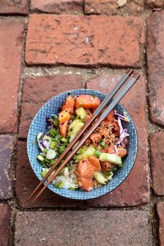 Raw salmon poke bowl with rice, cabbage, cucumber, sesame seeds and spring rolls with chopsticks.