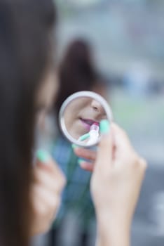young woman looking in the mirror and rouge her lips with red lipstick. Blurred background