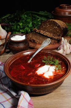 Borscht-vegetable beetroot soup, on the table with slices of rye cereal bread and gluten of sour cream, garlic and herbs. Rustic style.