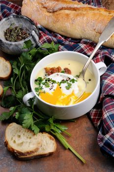 Garlic potato cream soup with bacon and poached eggs, herbs, spices