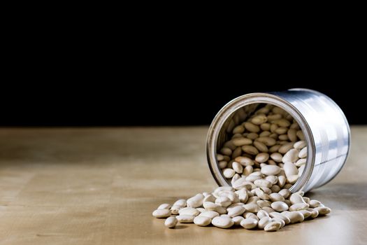 Delicious beans in a metal jar on a wooden kitchen table. Black background.